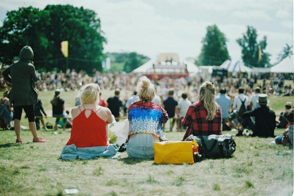 Individuals attending an outdoor concert sitting with backs to camera