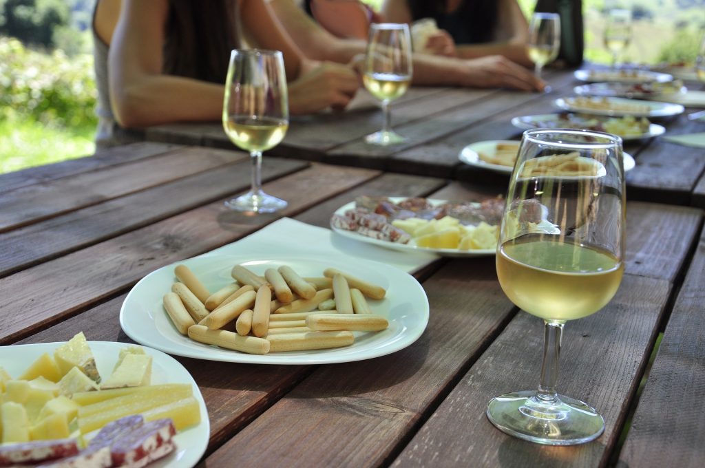 Outdoor table with plates of snack and several glasses of white wine