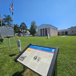 A historical wayside with a courthouse, green lawn and blue sky.