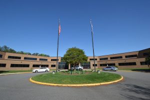 A two story brick building with a grass circle out front showcasing a tree, the American Flag and Chesterfield County Flag.