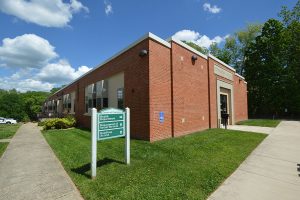 A one-story brick building with green grass and trees behind it.