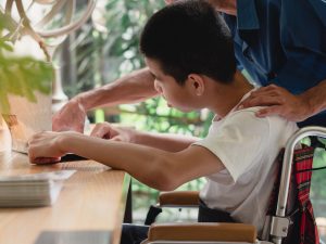 A person helps a teen in a wheelchair.