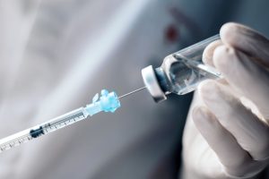 A hand holds a bottle with a syringe inserted.