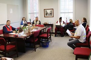 A group of people wearing vests sit around an office.