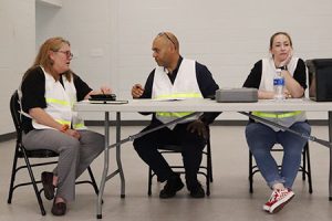 Three people wearing white vests sit at a table.