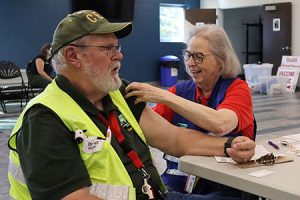 A person rolls up another person's sleeve in preparation for a vaccination.