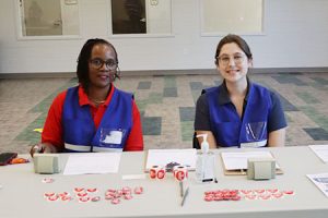 Two people sit behind a table with red buttons.