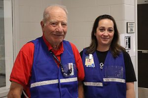 Two people wearing blue vests smile at the camera.